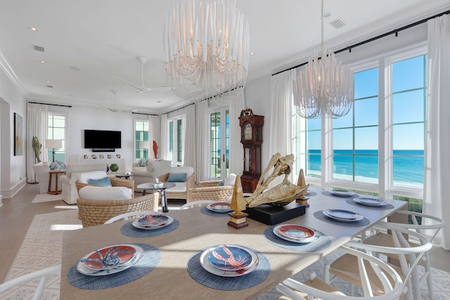 dining area with ceiling fan with notable chandelier, ornamental molding, light hardwood / wood-style flooring, and a water view