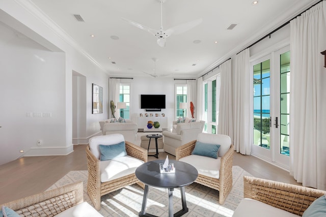 living room with french doors, ornamental molding, ceiling fan, and light wood-type flooring