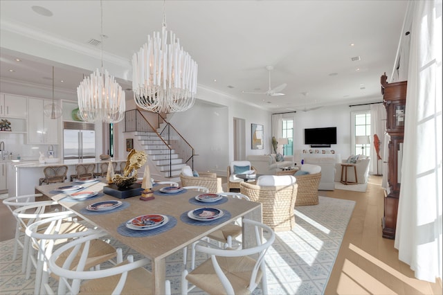 dining room featuring ceiling fan with notable chandelier, sink, ornamental molding, and light hardwood / wood-style flooring