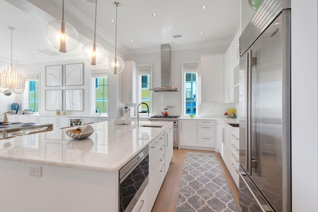 kitchen with white cabinetry, a kitchen island with sink, premium appliances, wall chimney range hood, and pendant lighting