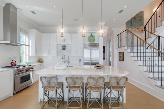 kitchen with white cabinetry, exhaust hood, an island with sink, and high quality appliances