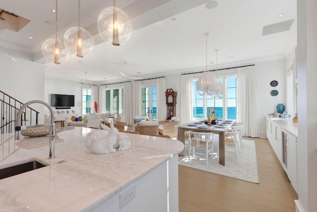 kitchen featuring light stone countertops, pendant lighting, a water view, white cabinets, and sink