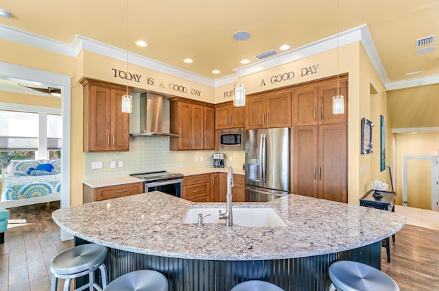 kitchen featuring wall chimney exhaust hood, a breakfast bar, stainless steel appliances, sink, and decorative light fixtures