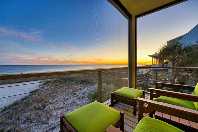 balcony at dusk with a water view and a view of the beach