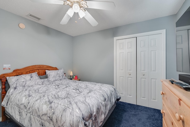 bedroom featuring a textured ceiling, dark colored carpet, ceiling fan, and a closet