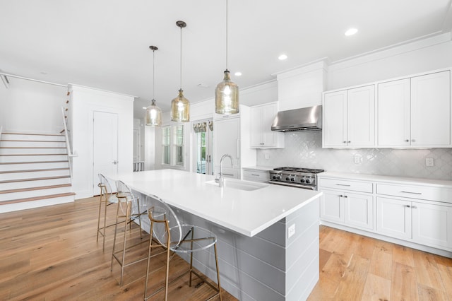 kitchen featuring white cabinets, sink, wall chimney range hood, and hanging light fixtures