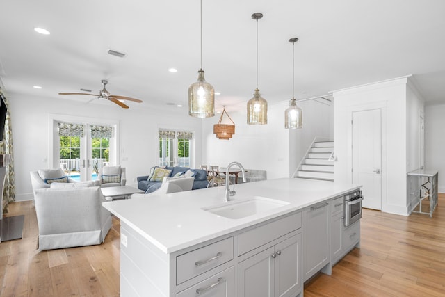 kitchen featuring stainless steel oven, a kitchen island with sink, sink, ceiling fan, and decorative light fixtures