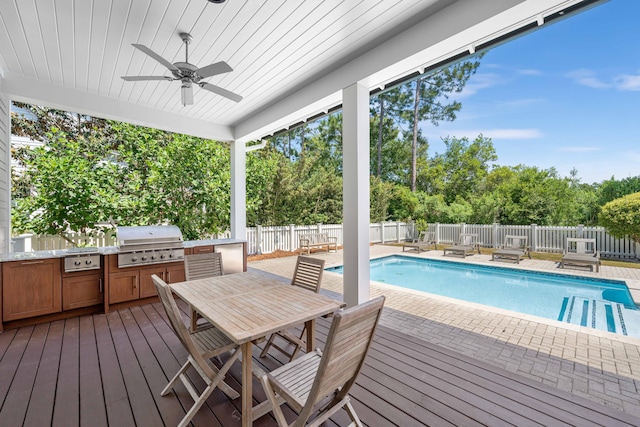 view of swimming pool featuring area for grilling, ceiling fan, a wooden deck, and exterior kitchen