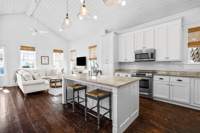 kitchen featuring a breakfast bar, a center island with sink, hanging light fixtures, white cabinetry, and stainless steel appliances