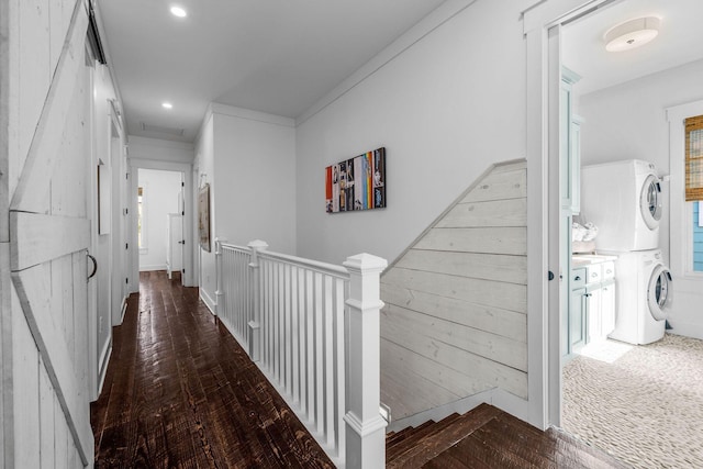 corridor with wooden walls, stacked washing maching and dryer, dark hardwood / wood-style floors, and crown molding