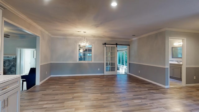 unfurnished dining area featuring ornamental molding, light wood-type flooring, a barn door, and an inviting chandelier