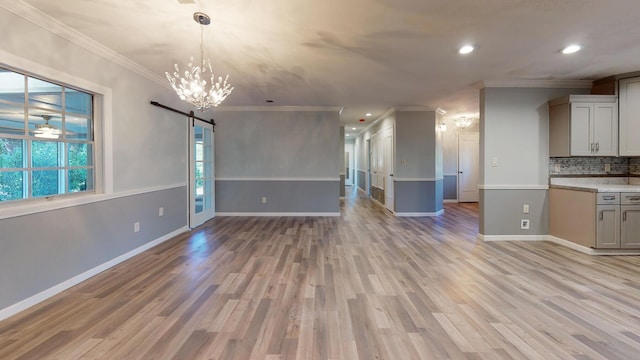 kitchen featuring a barn door, crown molding, light hardwood / wood-style flooring, an inviting chandelier, and tasteful backsplash