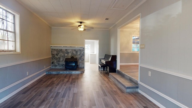 sitting room featuring ceiling fan, dark wood-type flooring, plenty of natural light, and a wood stove