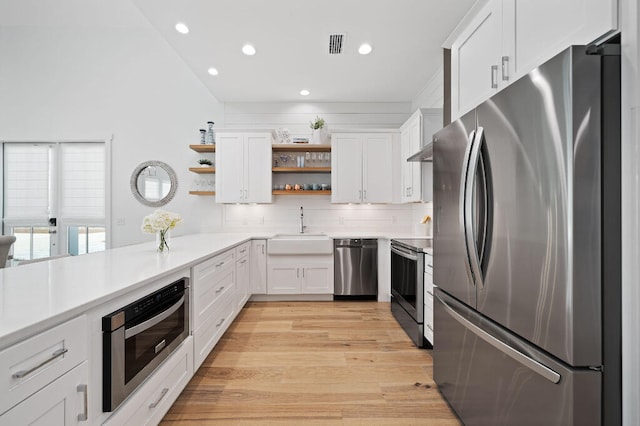 kitchen featuring appliances with stainless steel finishes, open shelves, a sink, recessed lighting, and light countertops