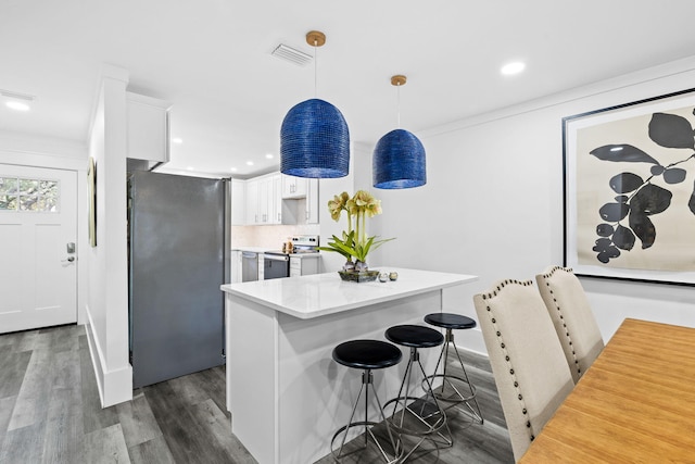 kitchen with dark wood-type flooring, a kitchen breakfast bar, pendant lighting, stainless steel appliances, and white cabinets