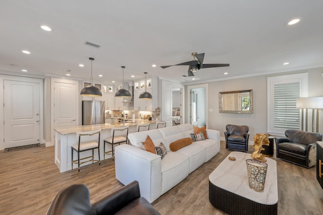 living room featuring ceiling fan, light hardwood / wood-style flooring, ornamental molding, and sink