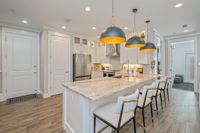 kitchen with white cabinets, pendant lighting, stainless steel appliances, and wall chimney exhaust hood