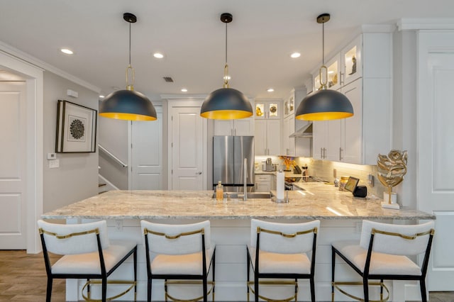 kitchen with stainless steel refrigerator, light stone counters, kitchen peninsula, crown molding, and white cabinets