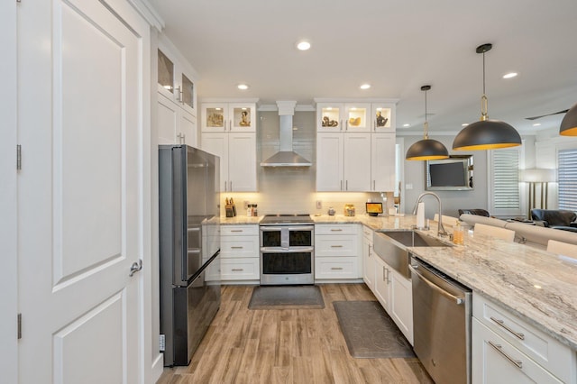 kitchen with pendant lighting, white cabinets, wall chimney range hood, sink, and stainless steel appliances