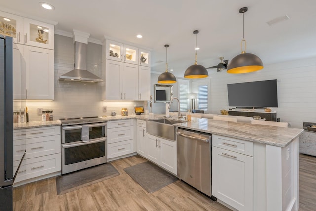 kitchen featuring pendant lighting, white cabinets, wall chimney range hood, appliances with stainless steel finishes, and light hardwood / wood-style floors