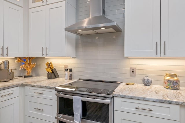 kitchen with backsplash, light stone counters, wall chimney exhaust hood, white cabinets, and stainless steel range with electric cooktop