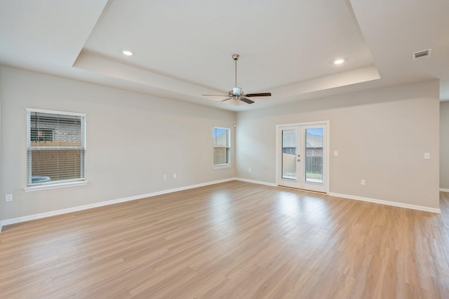 unfurnished room with a raised ceiling, ceiling fan, light hardwood / wood-style floors, and french doors