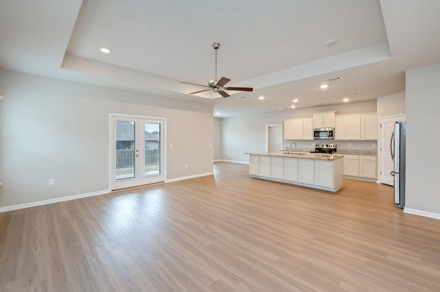 unfurnished living room featuring sink, a raised ceiling, and light hardwood / wood-style floors