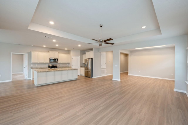 unfurnished living room with a raised ceiling, light wood-type flooring, and ceiling fan