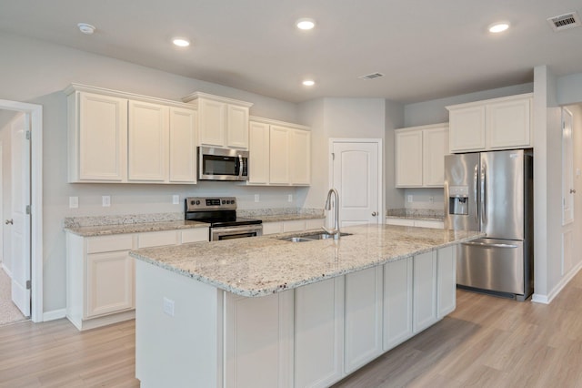 kitchen featuring light stone counters, stainless steel appliances, an island with sink, and sink