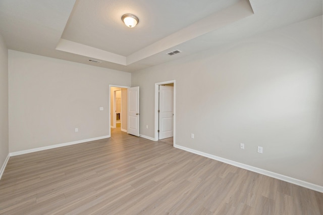 empty room featuring a raised ceiling and light hardwood / wood-style flooring