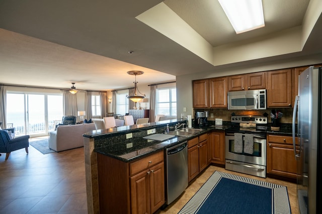 kitchen featuring a raised ceiling, kitchen peninsula, sink, hanging light fixtures, and stainless steel appliances