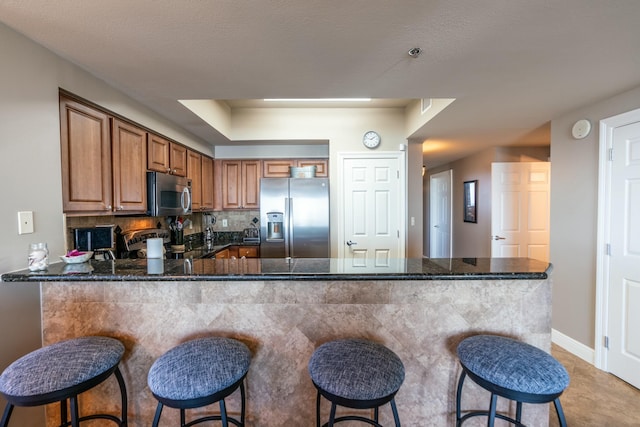 kitchen with a kitchen bar, kitchen peninsula, appliances with stainless steel finishes, decorative backsplash, and dark stone countertops