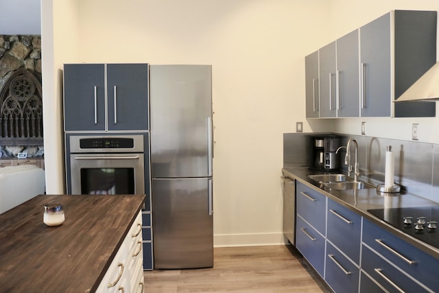 kitchen with sink, light hardwood / wood-style flooring, butcher block counters, stainless steel appliances, and extractor fan