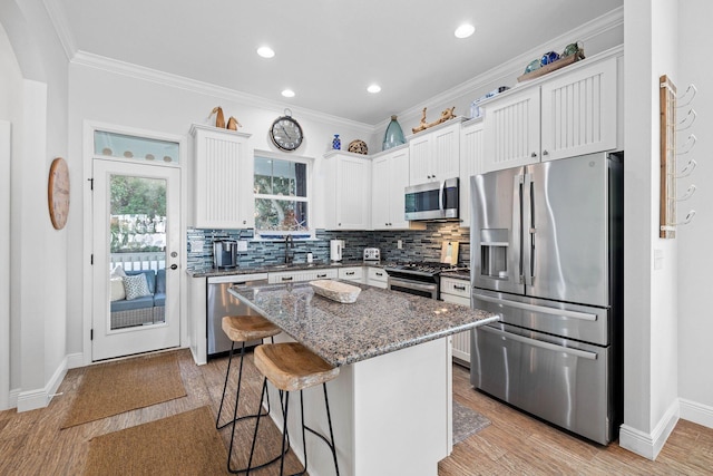 kitchen with a center island, dark stone counters, appliances with stainless steel finishes, white cabinetry, and a breakfast bar area