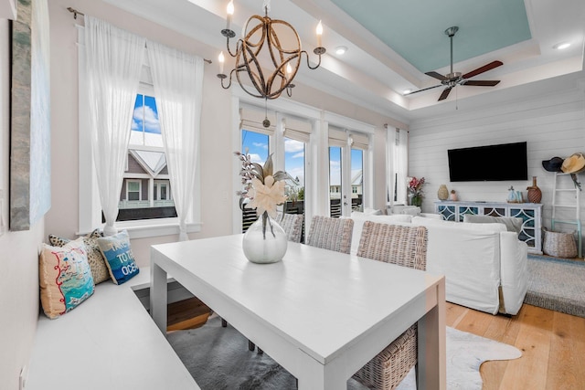 dining space with ceiling fan with notable chandelier, light wood-type flooring, and a raised ceiling