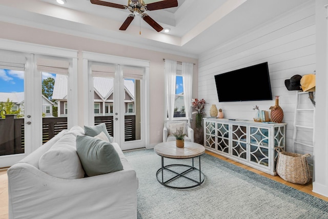 living room with french doors, light hardwood / wood-style floors, a raised ceiling, and wooden walls