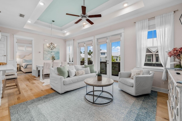 living room with ceiling fan with notable chandelier, light wood-type flooring, a raised ceiling, and ornamental molding