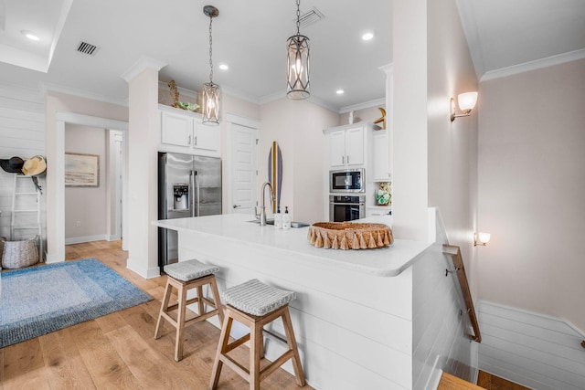 kitchen with a kitchen bar, white cabinetry, hanging light fixtures, and appliances with stainless steel finishes