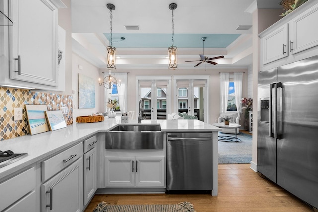 kitchen featuring kitchen peninsula, backsplash, stainless steel appliances, white cabinetry, and hanging light fixtures