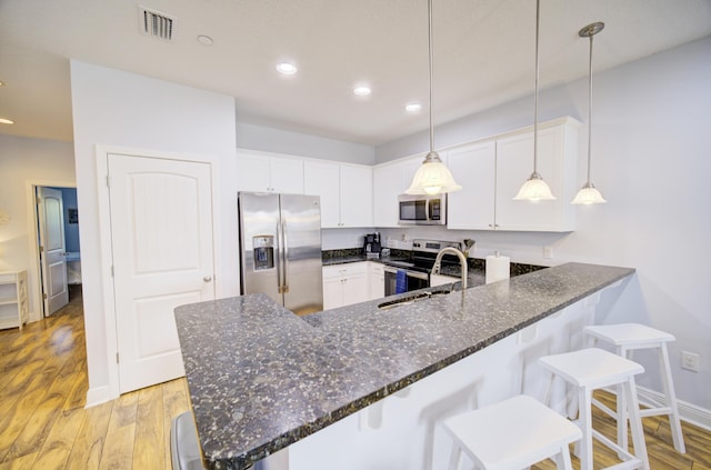 kitchen featuring kitchen peninsula, appliances with stainless steel finishes, sink, pendant lighting, and white cabinetry