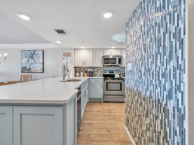 kitchen with visible vents, a peninsula, stainless steel appliances, light countertops, and a sink