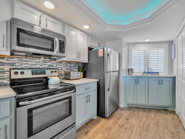 kitchen with stainless steel appliances, light wood-style floors, light countertops, backsplash, and a tray ceiling