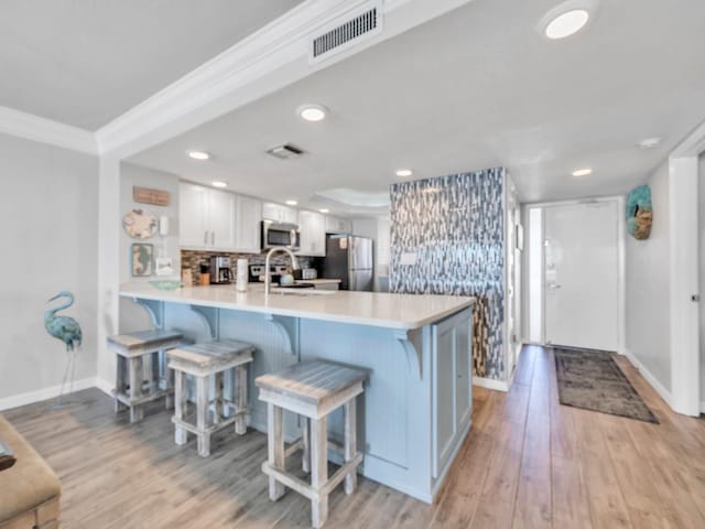 kitchen with visible vents, a kitchen breakfast bar, stainless steel appliances, light wood-style floors, and a sink