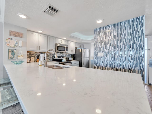 kitchen with a peninsula, visible vents, appliances with stainless steel finishes, backsplash, and a raised ceiling