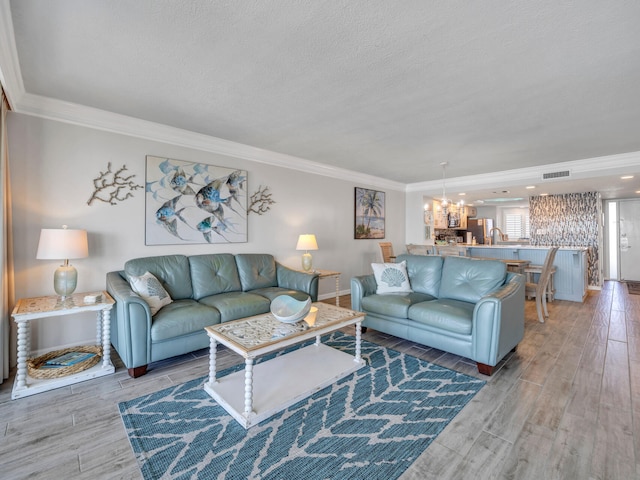 living room with a textured ceiling, visible vents, light wood-style floors, an inviting chandelier, and crown molding