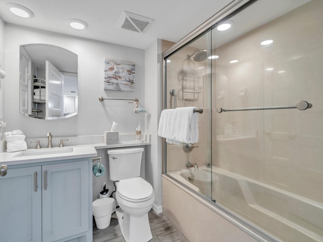 full bath with toilet, bath / shower combo with glass door, wood finished floors, vanity, and visible vents