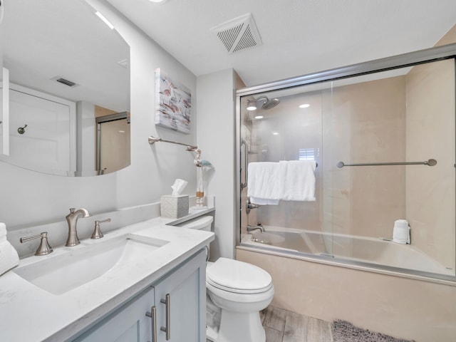 bathroom featuring visible vents, toilet, enclosed tub / shower combo, wood finished floors, and vanity