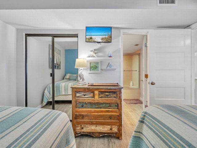 bedroom featuring a closet, wood finished floors, visible vents, and connected bathroom