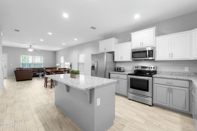 kitchen with ceiling fan, stainless steel appliances, a kitchen island, a kitchen bar, and white cabinets