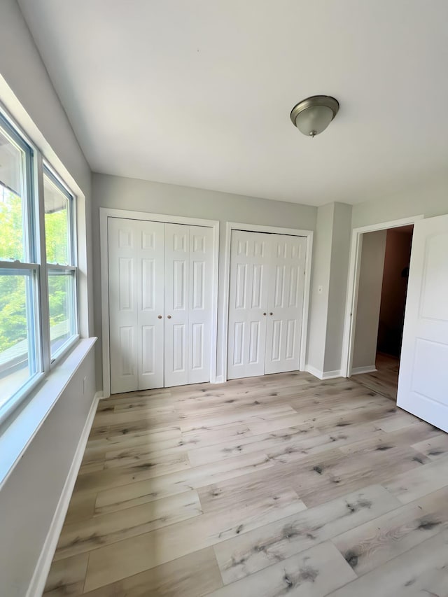 unfurnished bedroom with two closets and light hardwood / wood-style floors